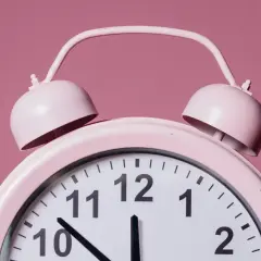 Różowy budzik z dzwonkami. Wskazówki pokazują godzinę 12, co w numerologii 12 symbolizuje początek i koniec.