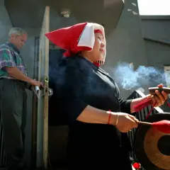 Kobieta w czerwono-białym nakryciu głowy, z kadzidełkami i gongiem, wykonuje rytuał. Czy to szaman kto to?
