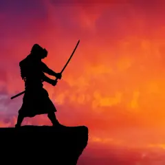 Samuraj w pozie bojowej, z dwoma mieczami w dłoniach, stoi na skraju klifu. Tło stanowi dramatyczne, ogniste niebo o zachodzie słońca.