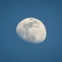 Jasny księżyc w wadze, z widocznymi kraterami, unosi się na tle granatowego nieba.