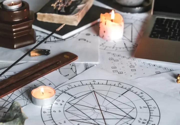Na stole leżą wykresy astrologiczne, świece, kadzidełko i laptop. Czas na obliczanie ascendentu.