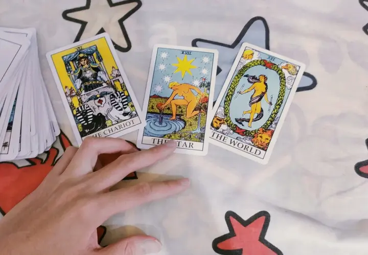 Dłoń wskazuje na karty Tarota: Rydwan, Gwiazda i Świat. Wygląda na to, że ktoś wybiera swoje 2 monety tarot.