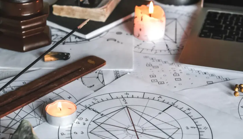 Na stole leżą wykresy astrologiczne, świece, kadzidełko i laptop. Czas na obliczanie ascendentu.