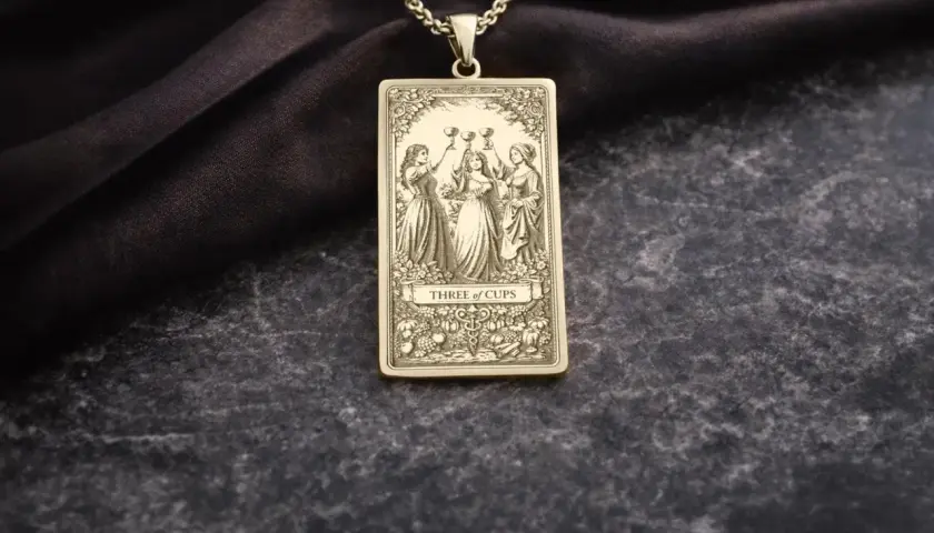 Złoty wisiorek z motywem 3 puchary tarot. Trzy kobiety wznoszą kielichy, celebrując radość i wspólnotę.