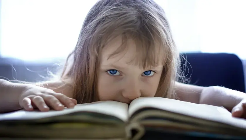 Mała dziewczynka z niebieskimi oczami pochyla się nad książką. Jej włosy opadają na otwartą księgę, tworząc magiczny obraz, jakby świat indygo dzieci otwierał się przed nią.