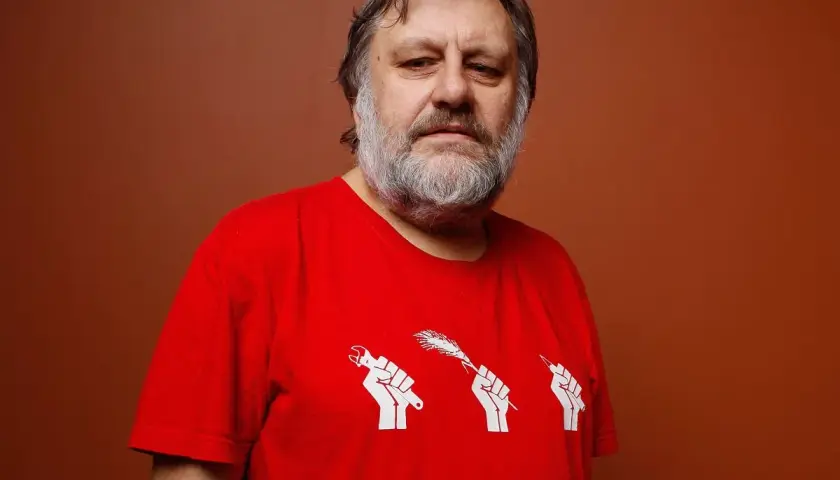 Mężczyzna z siwą brodą w czerwonej koszulce z symbolem trzech pięści trzymających narzędzia. Numerologiczna 33 mężczyzna, filozof.