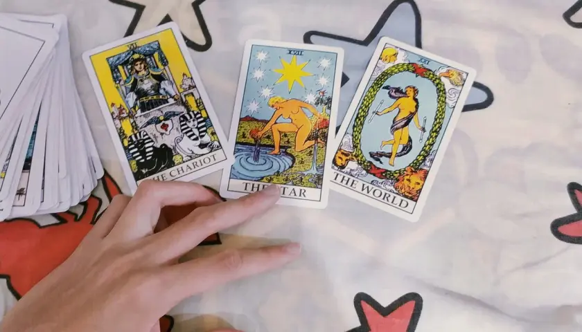 Dłoń wskazuje na karty Tarota: Rydwan, Gwiazda i Świat. Wygląda na to, że ktoś wybiera swoje 2 monety tarot.