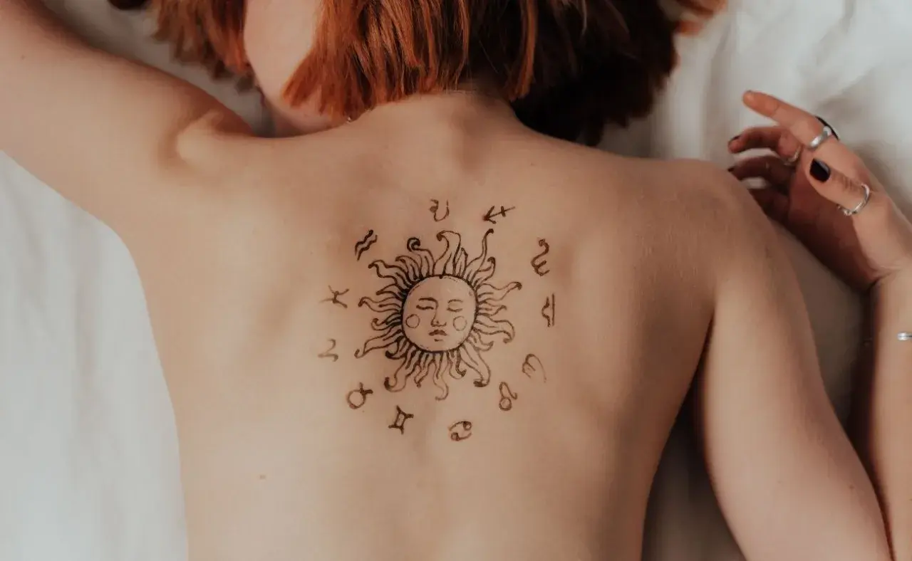 Tatuaż słońca z symbolami zodiaku na plecach. Może to symbolizować ascendent w Koziorożcu, wskazując na determinację i ambicję.