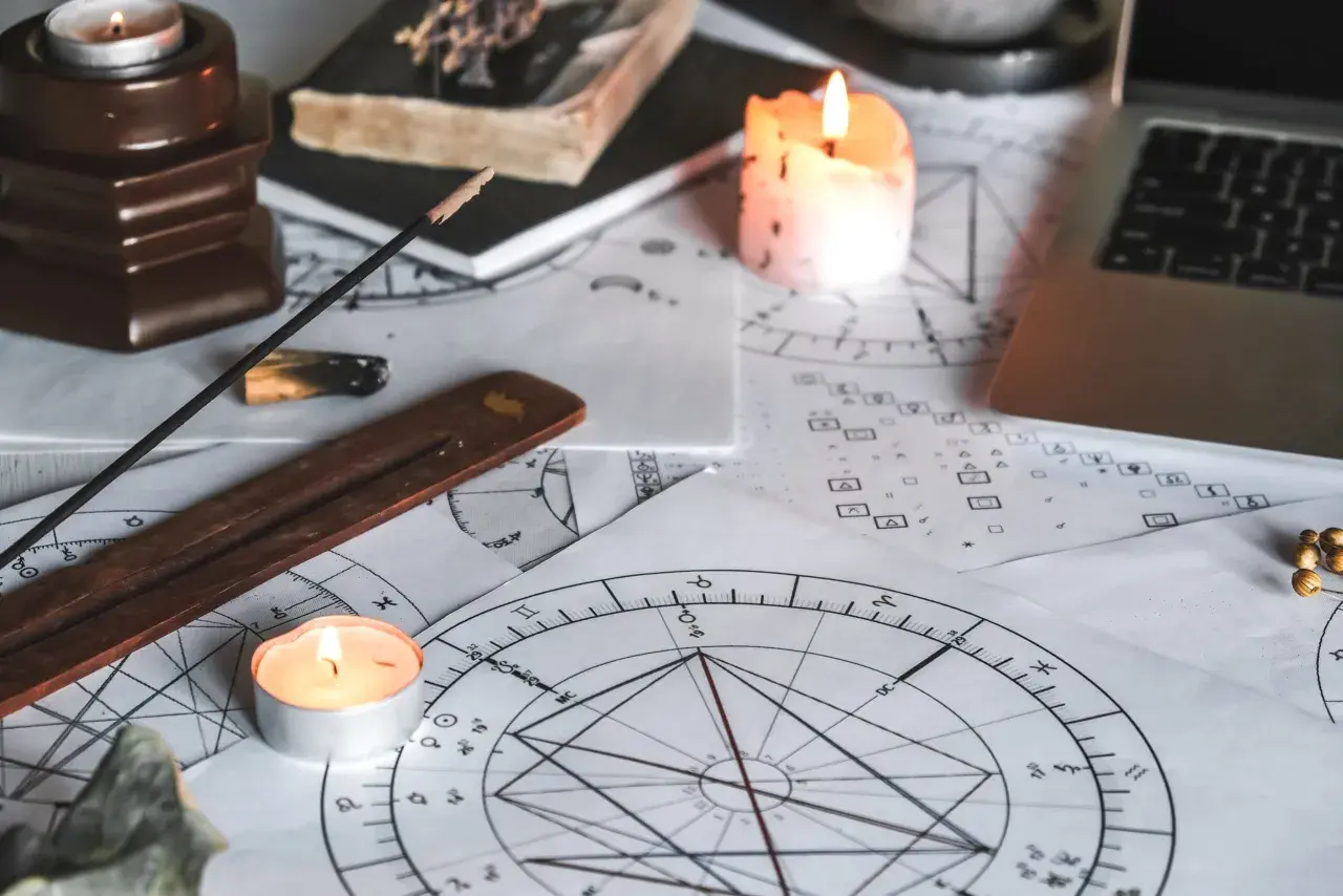 Na stole leżą wykresy astrologiczne, świece, kadzidełko i laptop. Czas na obliczanie ascendentu.