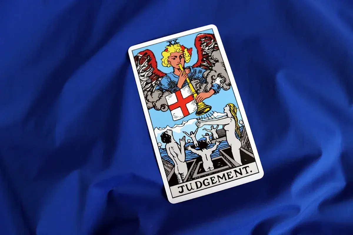 Karta Sąd Ostateczny z talii tarot. Anioł gra na trąbie, budząc ludzi z grobów.