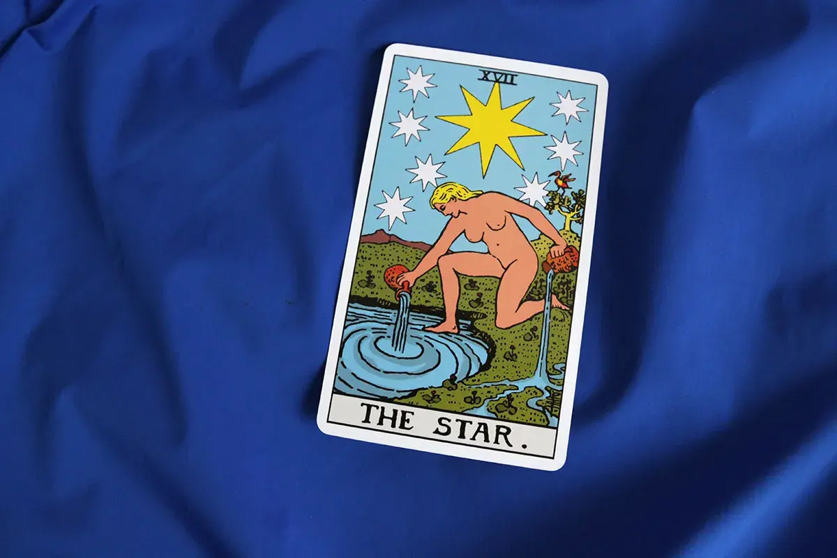 Karta Gwiazda Tarot symbolizuje nadzieję i spokój w uczuciach. Kobieta wylewa wodę, odnawiając życie.