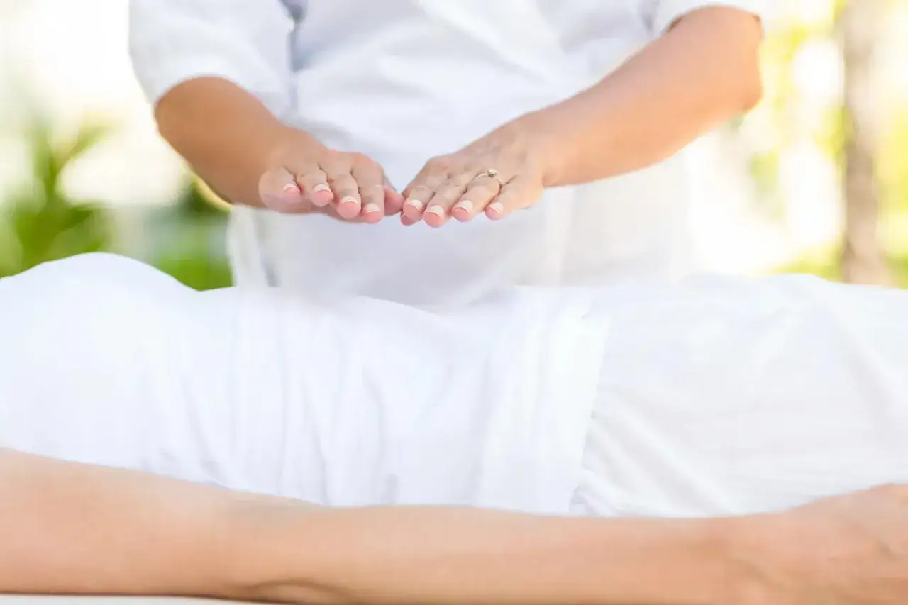 Dłonie terapeuty unoszą się nad ciałem osoby leżącej, wykonując zabieg reiki.